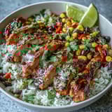 A vibrant Cajun Chicken Bowl is garnished with creamy avocado slices and lime wedges, ready for a zesty drizzle over the colorful Tex-Mex style ingredients.