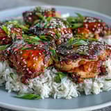 Savory-sweet honey garlic chicken thighs simmered until fall-apart tender, spooned over steaming rice with sesame garnish.  
