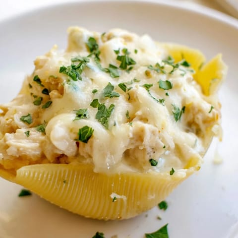 Golden-baked Chicken Alfredo Stuffed Shells sit in a ceramic dish, their cheese topping melted and bubbling with steam rising.  