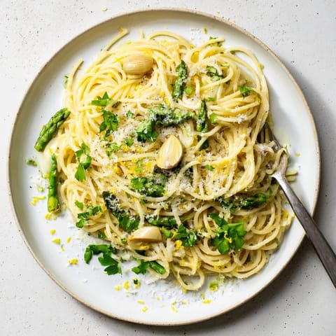 A close-up of Roasted Garlic & Asparagus Pasta, featuring golden roasted garlic cloves and vibrant green asparagus spears tossed in olive oil and Parmesan.