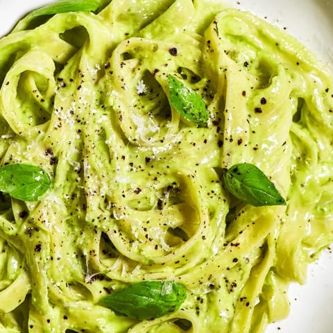 A skillet of Creamy Green Pea Alfredo is garnished with fresh basil and cracked black pepper. 