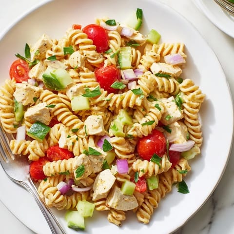A hearty, chilled pasta salad with golden chicken, cherry tomatoes, and cucumbers glistening in a zesty honey-mustard vinaigrette.