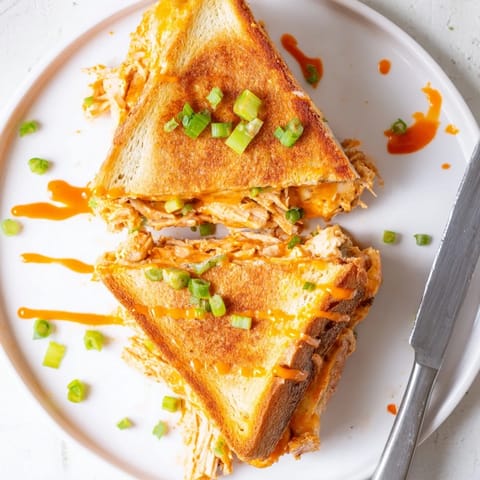 Gooey cheese pulls from a homemade Buffalo Chicken Ranch Grilled Cheese, served with crisp celery sticks for balance.