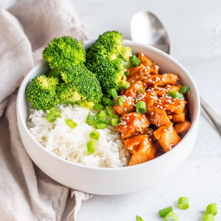 A close-up of a vibrant Sweet Chili Chicken Bowl garnished with green onions and sesame seeds.