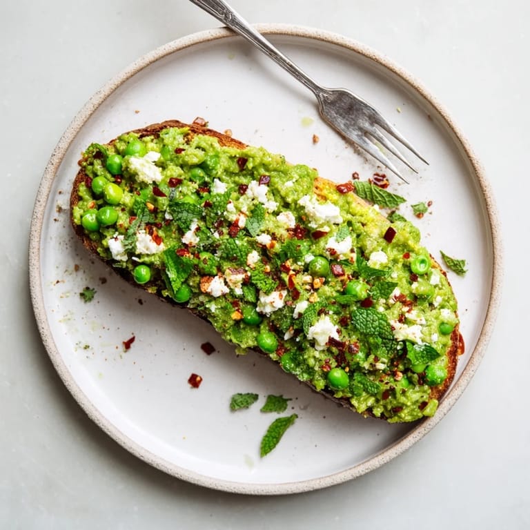 An open-faced sandwich featuring Smashed Pea & Chicken Toast, topped with crumbled feta and a squeeze of lemon for brightness.