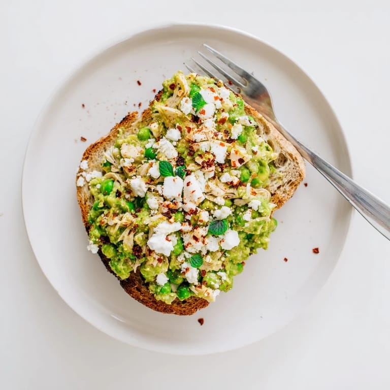 A close-up of a crispy Smashed Pea & Chicken Toast, showcasing the chunky green spread and tender shredded chicken on rustic bread.