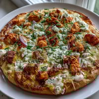 Golden-brown Buffalo Chicken Pizza topped with melted mozzarella, cheddar, spicy buffalo chicken, red onion slices, and fresh chives on a wooden table.