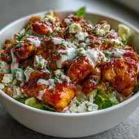 Spicy buffalo chicken bowl with tender chicken, crisp veggies, and creamy ranch dressing, topped with tangy blue cheese crumbles.