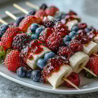 Festive Fourth of July fruit skewers with strawberries, bananas, and blueberries in patriotic red, white, and blue pattern.